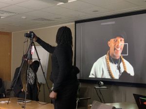 Image of facilitator Adisa being photographed by a student and projected onto a screen